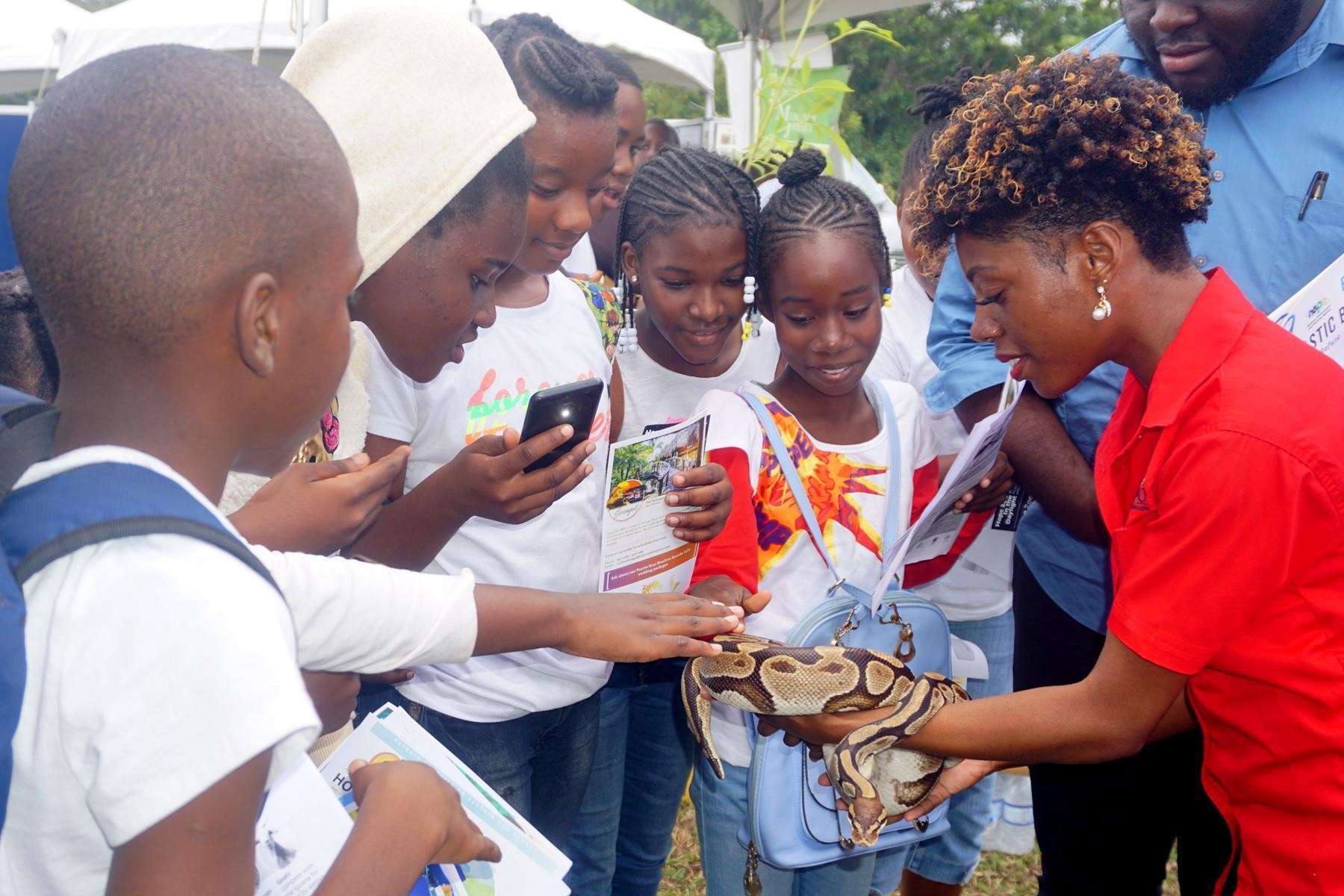 Curious students interacting with a live Jamaican 
Yellow Snake at the Hope Zoo’s Booth with Shaneek Lewis